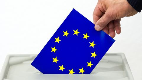 Hand wirft Stimmzettel mit EU-Logo in eine Wahlurne