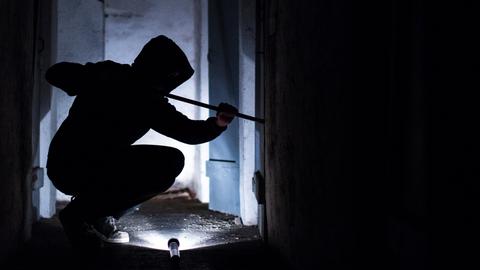 Ein fiktiver Einbrecher hebelt mit einem Brecheisen eine Tür im Keller eines Wohnhauses auf