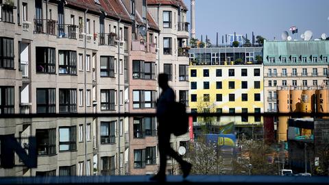 Ein Mann geht vor der Kulisse von innerstädtischen Wohnhäusern über eine Brücke.