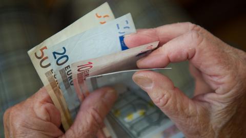 Älter aussehende Hände halten mehrere Euronoten in der Hand und zählen das Geld.