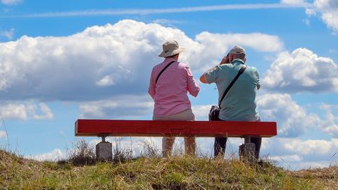 Zwei ältere Personen sitzen auf einer Bank, die auf einem Hügel im Nationalpark Unteres Odertal steht.