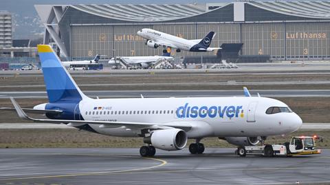 Während eine Maschine der Lufthansa startet, wird ein Passagierflugzeug der Discover Airlines am Frankfurter Flughafen von einem Schlepper gezogen.