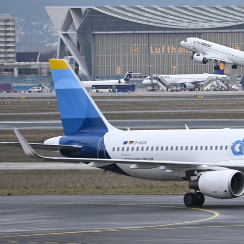 Während eine Maschine der Lufthansa startet, wird ein Passagierflugzeug der Discover Airlines am Frankfurter Flughafen von einem Schlepper gezogen.