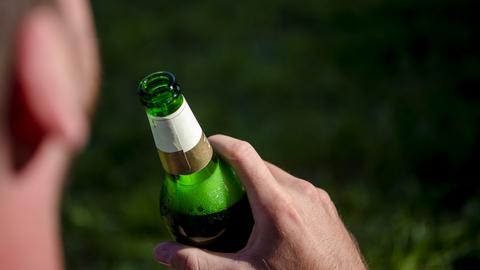 Ein Mann sitzt im Olympia-Park in München und trinkt aus einer Flasche Bier (Archivbild). 