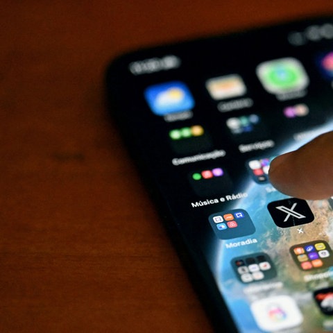 Ein Smartphone-Nutzer wählt mit seinem Finger die App der sozialen Plattform X an. 