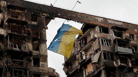 Eine zerrissene ukrainische Flagge hängt an einem Draht vor einem Wohnhaus, das während des russischen Angriffskrieges in der südukrainischen Hafenstadt Mariupol am 14. April 2022 zerstört wurde.