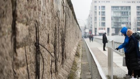 Touristen betrachten  an einem Stück der ehemaligen Berliner Mauer eine Informationstafel.