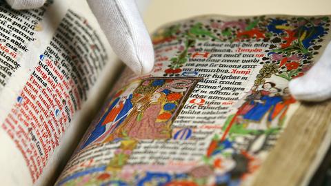 Eine Archivarin blättert in Köln (Nordrhein-Westfalen) in einem reich ausgemalten Gebetbuch.