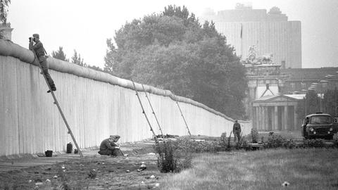 Grenzsoldaten der DDR sitzen hinter der Berliner Mauer.