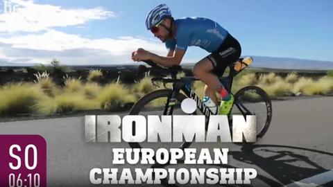 Ein Teilnehmer im Trikot und mit Helm auf einem Rennrad fährt schnell eine aphaltierte Straße entlang, im Hintergrund hügelige Landschaft. Über dem Motiv der Schriftzug "Ironman European Championchip"