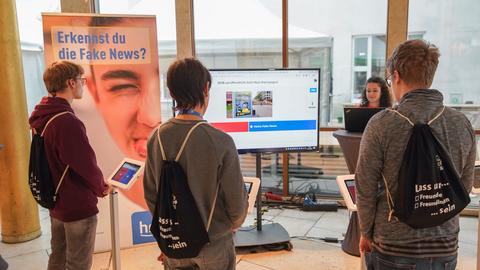 Schüler stehen in der Goldhalle an kleinen Bildschirmen und machen ein Quiz zum Thema "Fake News".