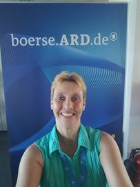 Angelika Chaluppa vor einer blauen Wand mit der Aufschrift "Börse ARD"