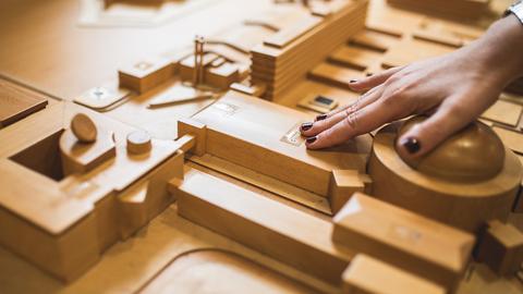 Ein aus Holz gefertigter taktiler Lageplan mit den Gebäuden des hr, dazu Beschriftung in Braille. In Großaufnahme eine Hand, die fühlt.