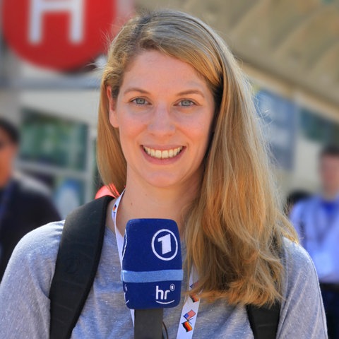 Katharina Wilhelm hält ein Mikrofon in der Hand und steht auf der Straße