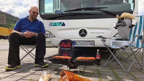 Onkel Otto trägt einen Hut und grillt mit einem Bekannten auf dem Messeparkplatz in Marburg.