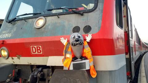 Onkel Otto trägt eine Warnweste und steht vo einer Regionalbahn