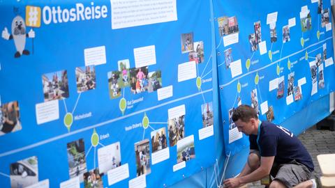 Ein hr-Mitarbeiter spannt ein Banner mit Bildern von Onkel Ottos Reise zum Hessentag auf.