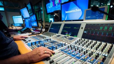 Ein Mitarbeiter sitzt an der Bildregie eines Fernsehstudios und schaut auf Monitore, vor sich hat er viele Regler.