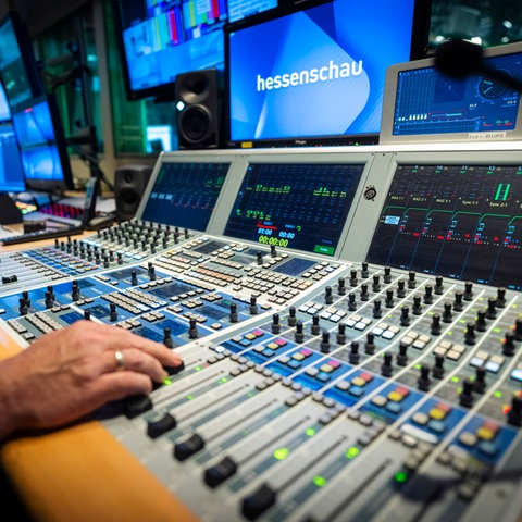 Ein Mitarbeiter sitzt an der Bildregie eines Fernsehstudios und schaut auf Monitore, vor sich hat er viele Regler.